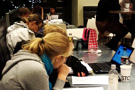 Studenter i en högskolekafeteria pluggar vid sina laptops.