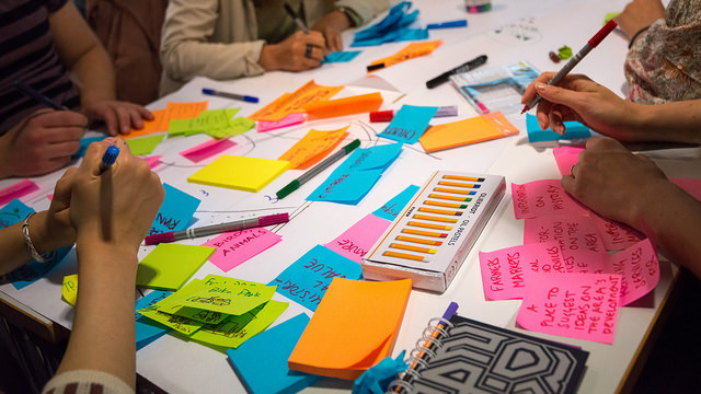 En grupp som jobbar runt ett bord fullt med färgglada postit-lappar som de skriver på.