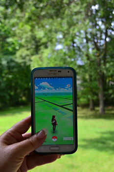 Hand som håller en mobil med PokemonGo på skärmen. Ett skogsområde i bakgrunden.
