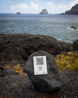 QR-kod fäst på en sten som ligger på klipporna i ett narurområde vid kanten av ett hav.