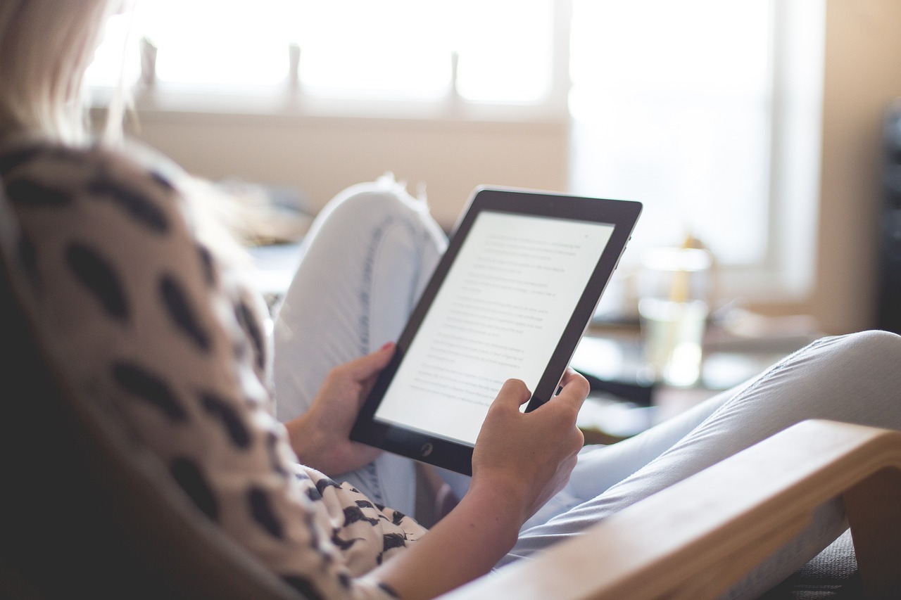 En kvinna som sitter bekvämt i en fåtölj med en iPad i knäet.