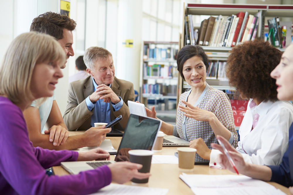 En grupp äldre studenter sitter runt ett bord i ett bibliotek och diskuterar.