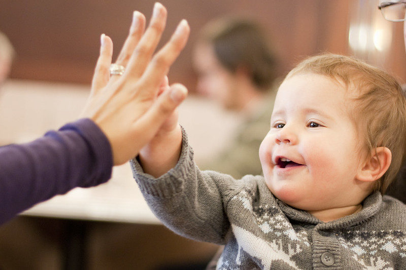 En glad baby gör en high-five med en vuxen.